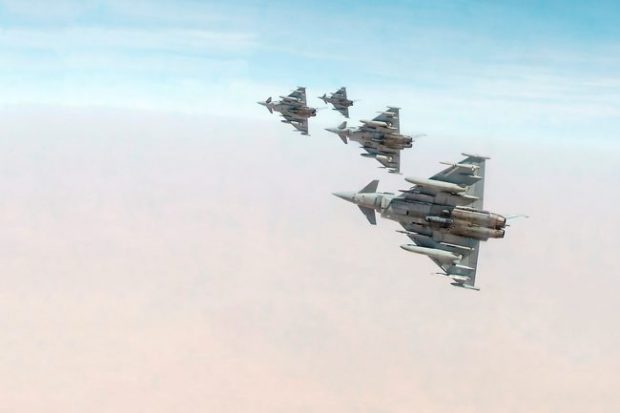 The image shows four triangular shaped fighter jets against a pinky-blue sky