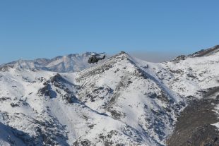 An RAF Puma Helicopter flying above a snowy hill