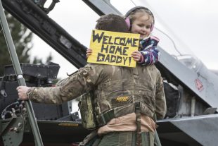 Squadron Leader Bonning descending the steps of a Tornado aircraft whilst holding his daughter.