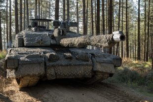 A British Army tank adorned with camouflage in a forest 