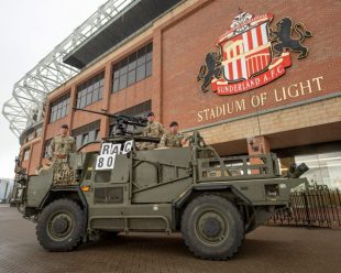 A British army Jackal and its crew parade next to Sunderland A.F.C The Stadium of Light football ground.