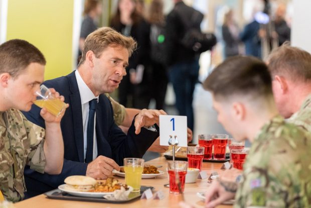 Tobias Ellwood sits at a table eating lunch with uniformed soldiers