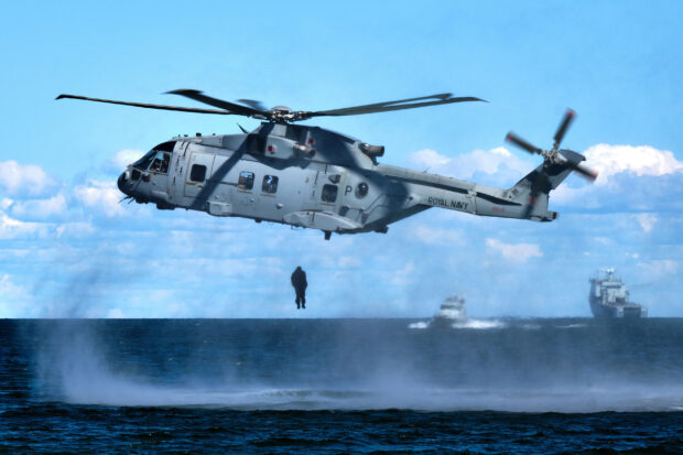 A helicopter hovers low over the sea as a Royal Marine hangs beneath it from a rope