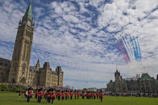 The Red Arrows fly in formation over the peace tower and a military parade as they change the guard in Ottawa, leaving a red white and blue jet trail behind them