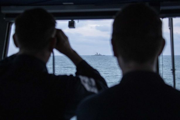 Royal Navy sailors watch a Russian ship pass them from HMS Mersey